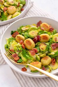 Close up shot of the plate of sautéed Brussel sprouts, crispy gnocchi and bacon. Gold fork tucked under some of the food inside the plate.