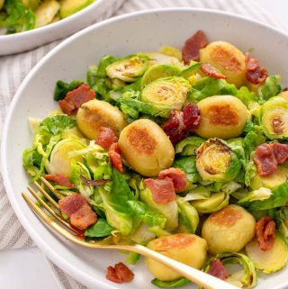 Close up shot of the plate of sautéed Brussel sprouts, crispy gnocchi and bacon. Gold fork tucked under some of the food inside the plate.