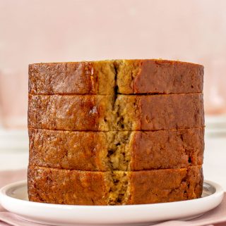 Stack of four thick slices of banana bread on a white plate. Plate is sitting on a pink napkin.