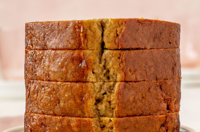 Stack of four thick slices of banana bread on a white plate. Plate is sitting on a pink napkin.
