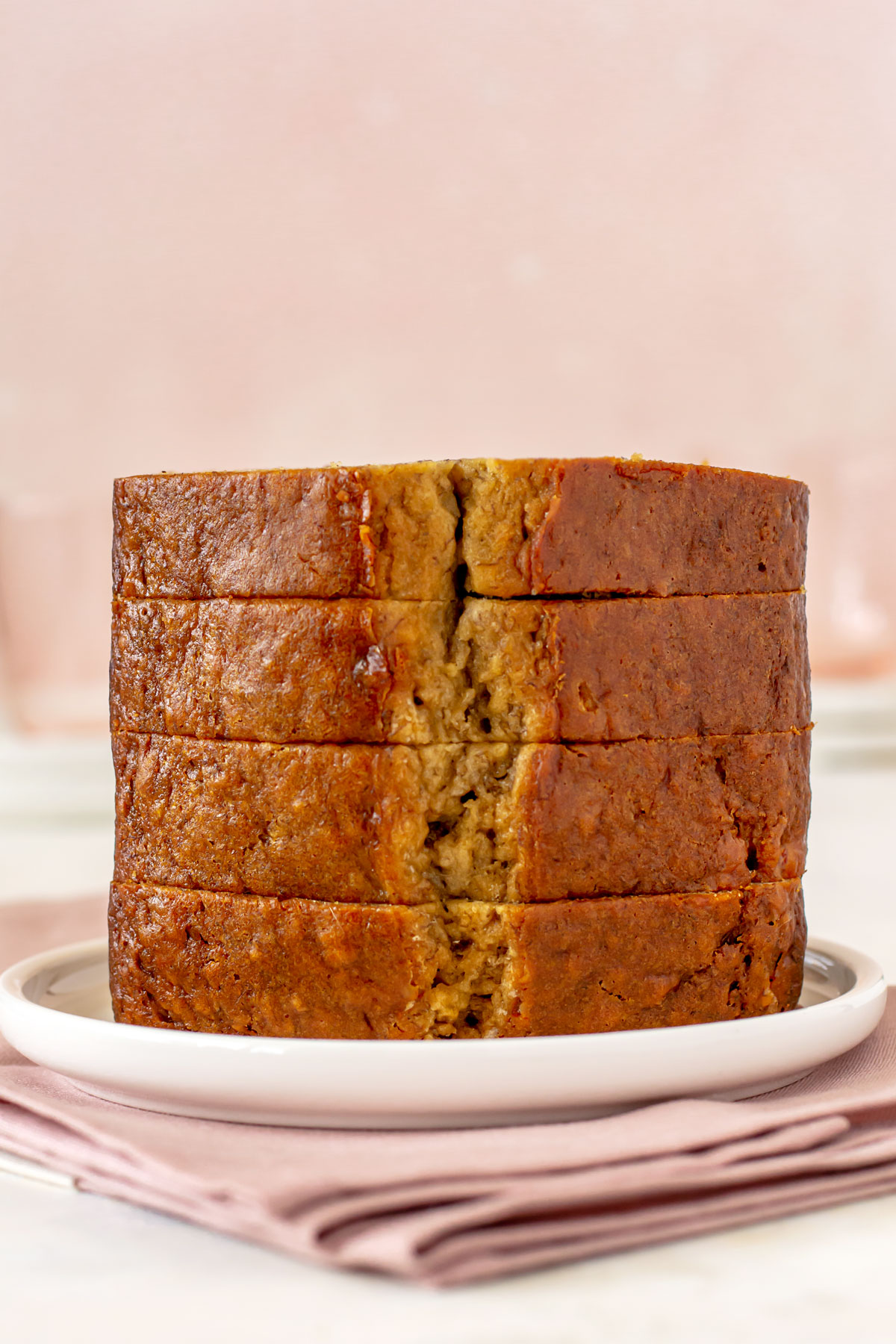 Stack of four thick slices of banana bread on a white plate. Plate is sitting on a pink napkin.