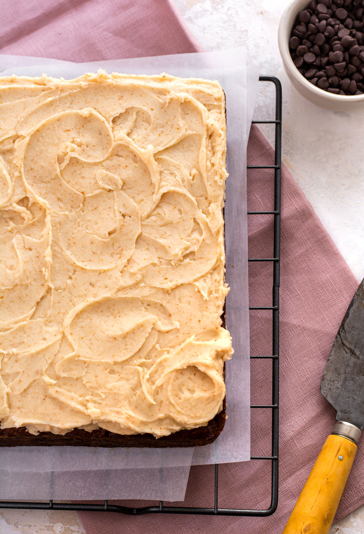 Top down shot of the whole banana cake with frosting. Small bowl of mini chocolate chips in top right corner.