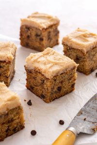 Close up of a square of cake with frosting, showing the mini chocolate chips inside the cake.