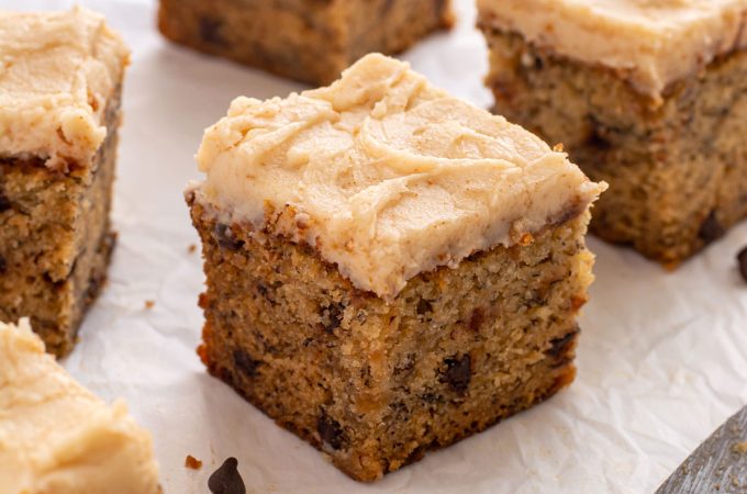 Close up of a square of cake with frosting, showing the mini chocolate chips inside the cake.